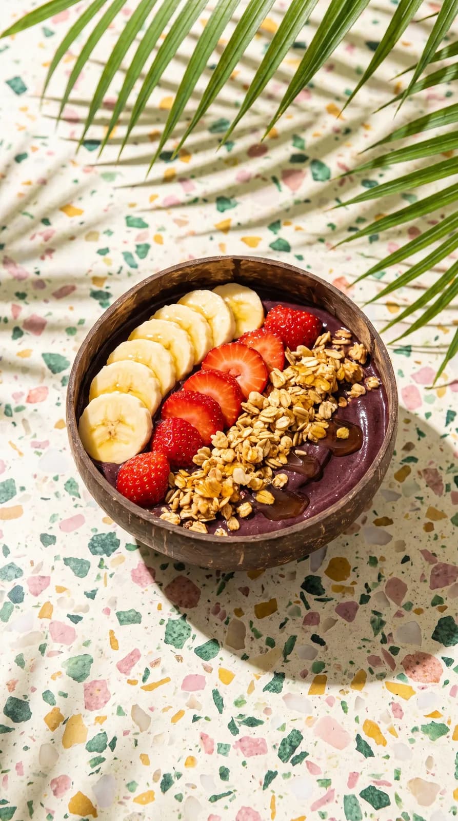 Tigela de açaí com banana, morango e granola sobre bancada de granilite ao sol