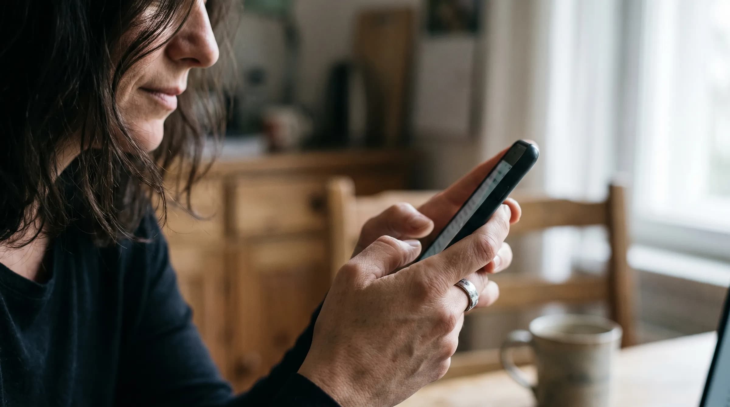 Pessoa usando o celular em casa, com uma xícara sobre a mesa ao lado