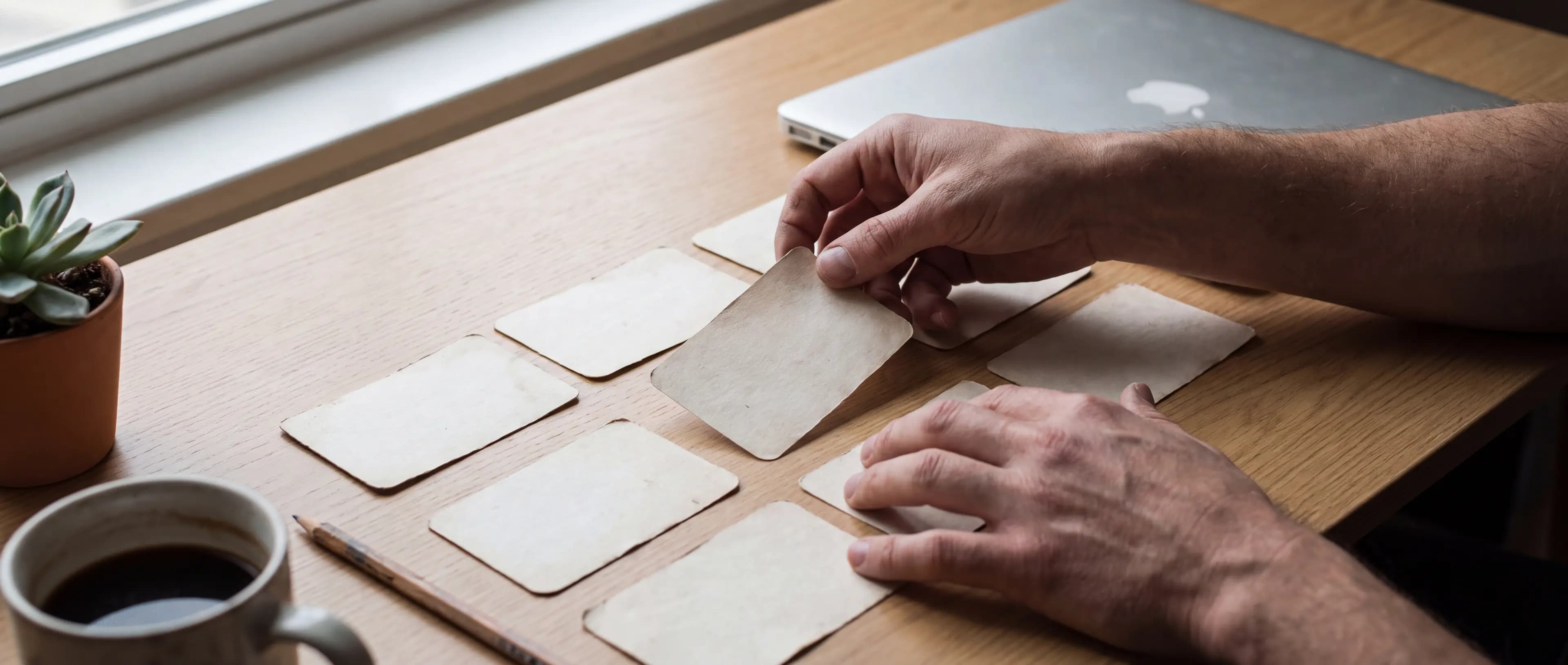 Mãos organizando cartões de papel em grade sobre uma mesa de madeira clara