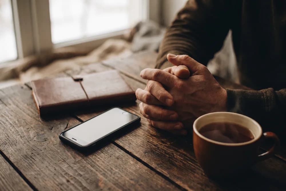 Mãos ao lado do celular e de um caderno sobre a mesa de casa
